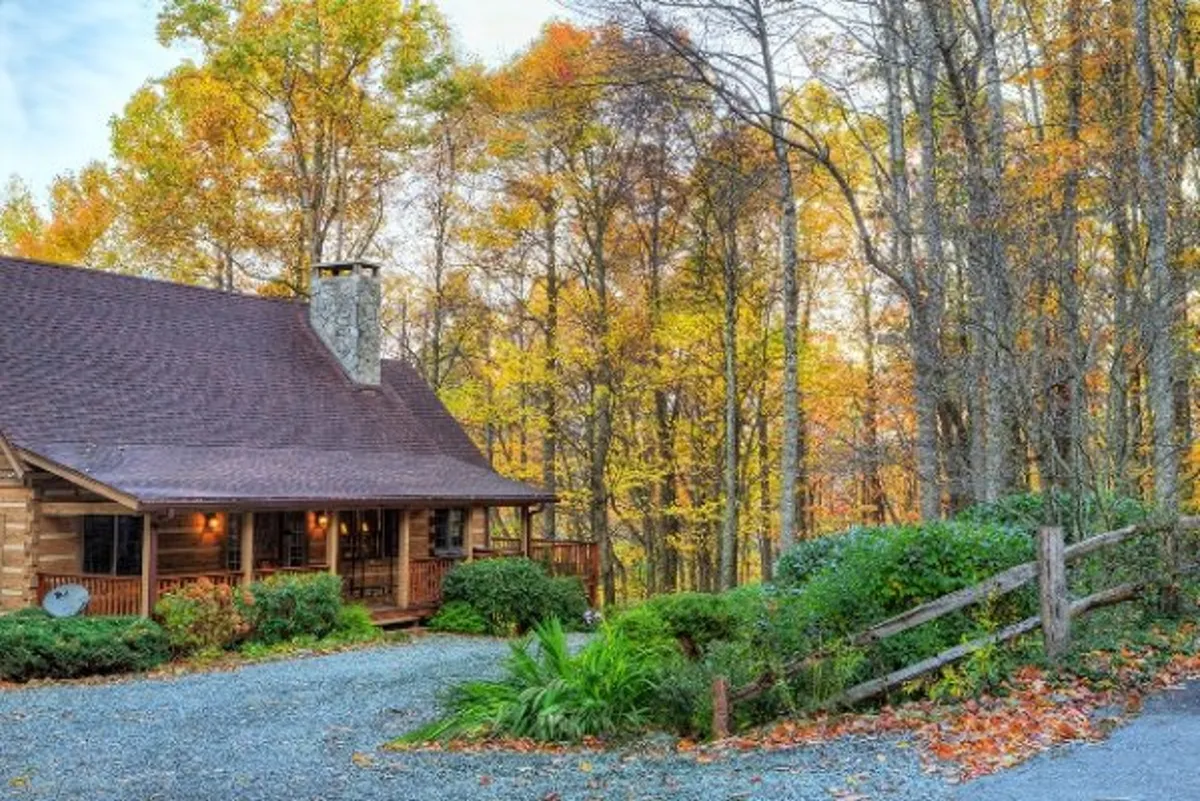 This image captures the log cabin's welcoming facade, surrounded by vibrant autumn foliage. The stone chimney and the driveway set the scene for easy outdoor access, while the porch hints at relaxing moments after a day of adventure.