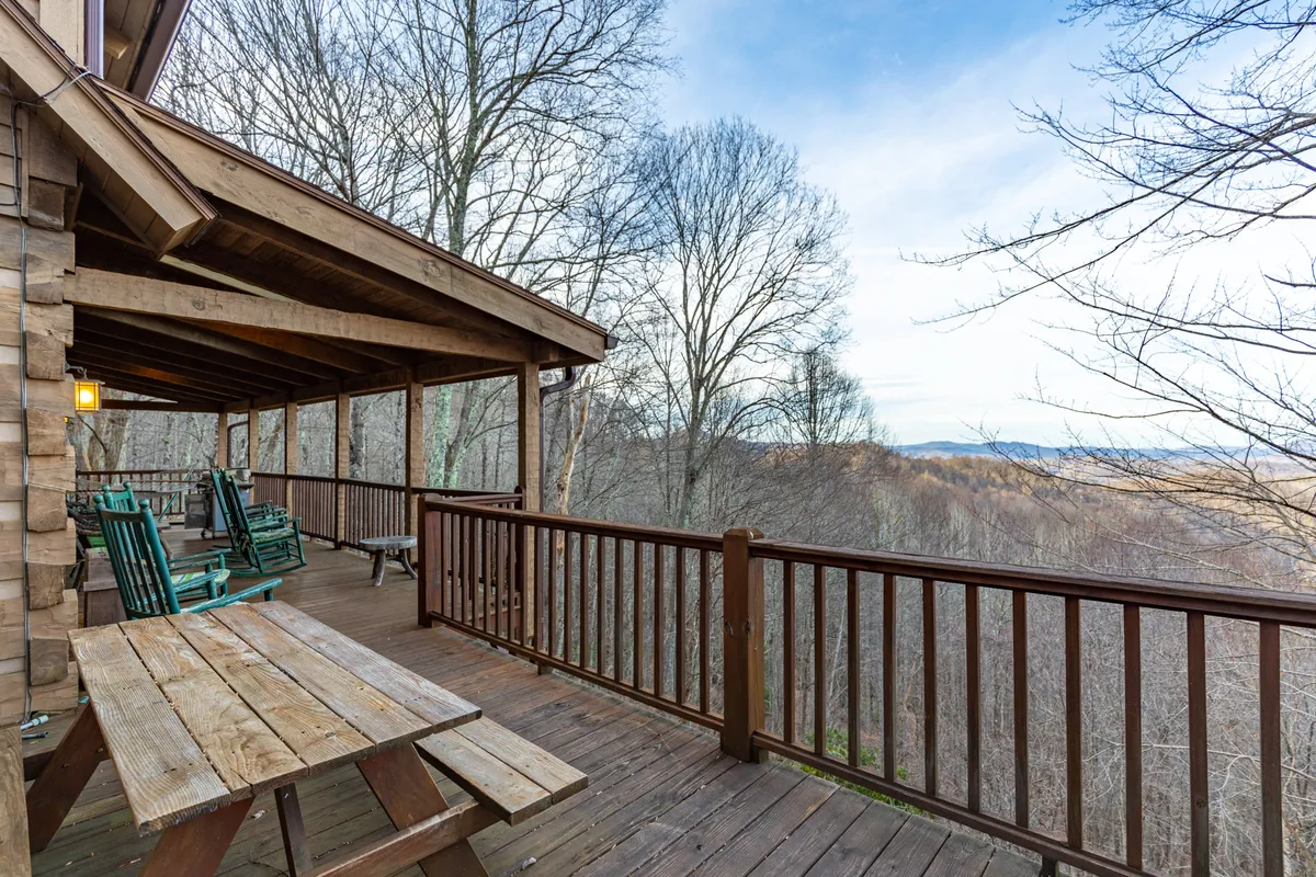 A serene outdoor area featuring a spacious wooden deck furnished with classic rocking chairs, a table, and a stunning mountain view beyond. The scene is set up for socializing, outdoor dining, or simply enjoying the beauty of nature with loved ones.