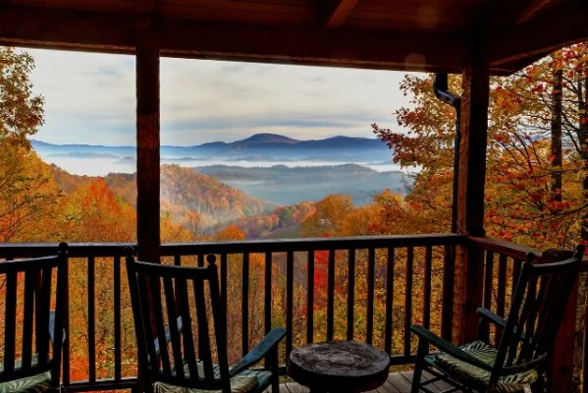 A pair of classic wooden rocking chairs sit on a wooden deck overlooking distant mountains painted in fall hues. The scene is serene and inviting, perfect for soaking in sunrise views or unwinding after a day on the trails.