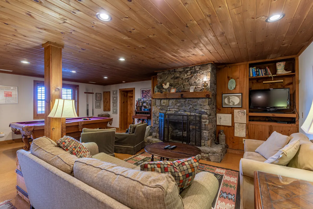 A welcoming recreation room featuring a cozy fireplace, plush seating, a pool table, and a bookshelf. The space is designed for both spirited games and relaxed gatherings, with warm lighting and rustic decor enhancing the inviting atmosphere.