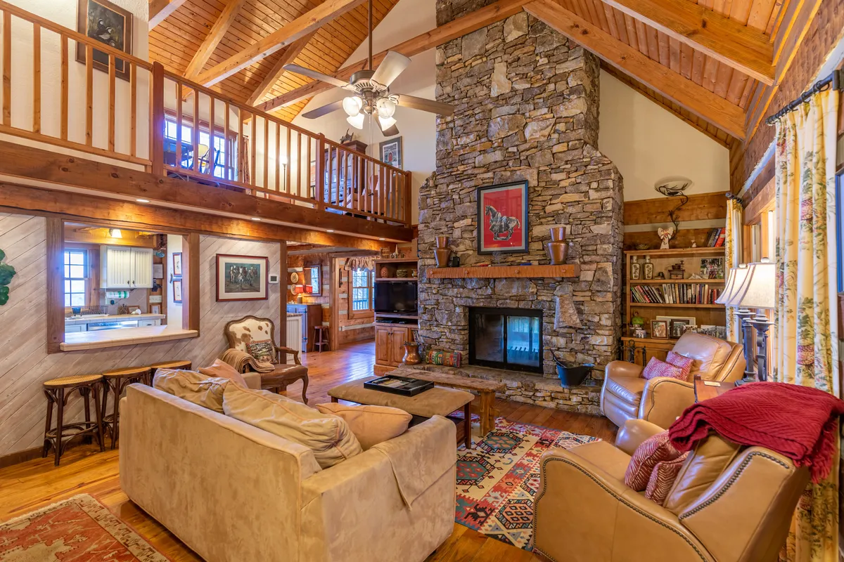 A cozy interior scene with a stone fireplace, comfortable seating, rustic wooden beams, and an open area ideal for conversation and connection. The space is bathed in warm light, evoking a sense of comfort and relaxation—ideal for family gatherings or quiet moments by the fire.