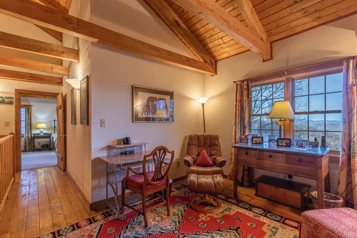 A warm, inviting loft space with wooden beams, a recliner chair, a desk with a lamp, and framed pictures. The desk area is ideal for reading, relaxing, or remote work, aligning with the section’s mention of WiFi in the loft.
