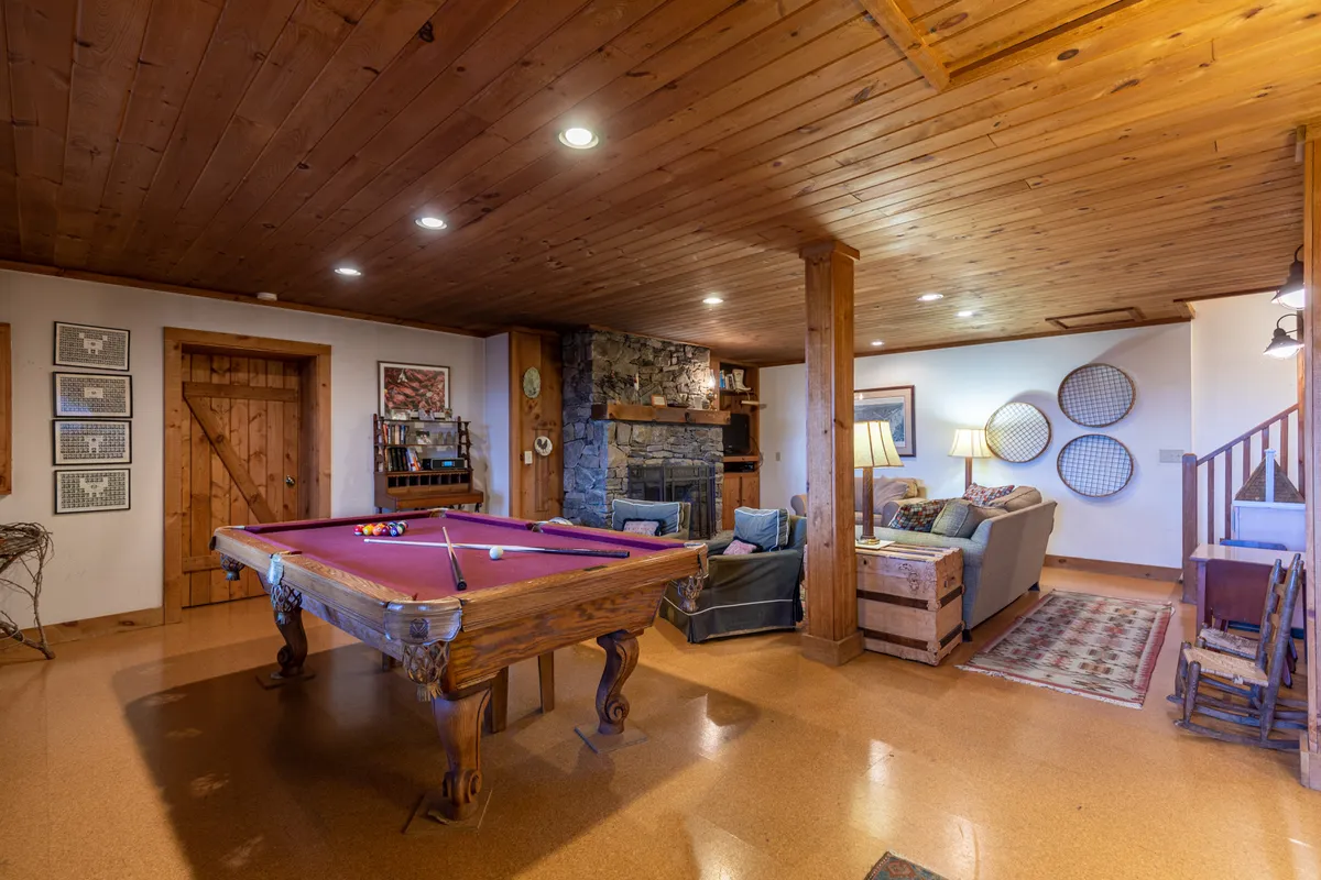 A vibrant recreation room featuring a pool table, stone fireplace, comfortable seating, and wooden beams. The space is designed for fun and connection, perfect for game nights or relaxing by the fire after a day of exploration.